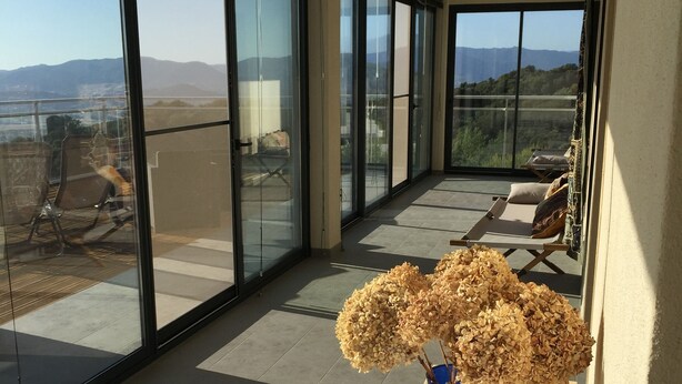 A balcony with a wooden table and a vase of dried flowers, large glass doors, and a view of the landscape. - Bedroom ADVENTURE Villa AMALIA (PORTICCIO)
