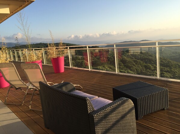 A wooden deck with wicker furniture and potted plants, overlooking a forested landscape. - Bedroom ADVENTURE Villa AMALIA (PORTICCIO)