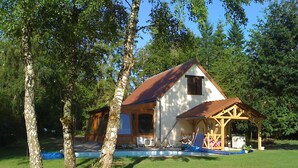 A rustic cabin with a wooden porch and a small attached structure, surrounded by trees.