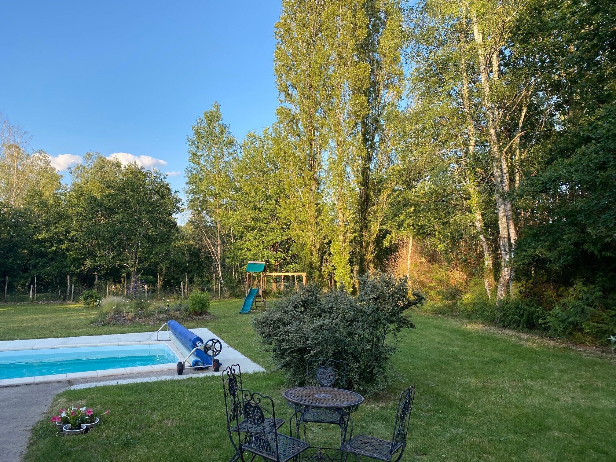A backyard with a swimming pool, a slide, a table with chairs, and a small garden.