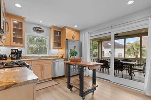 A kitchen with wooden cabinets, a refrigerator, a coffee maker, and a dining area with outdoor seating.