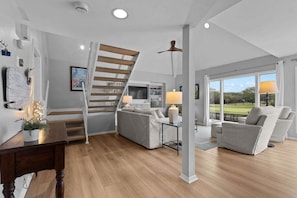 A modern living room with a staircase, a sofa set, a dining table, and a view of the outdoors.