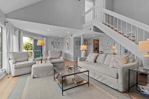 A spacious living room with a high ceiling, a staircase, and a balcony with curtains.