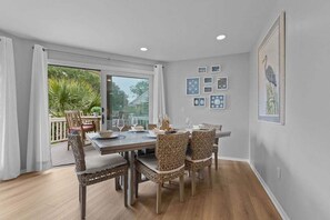 A dining area with a table set for four, wicker chairs, and a view of greenery outside.