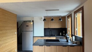 A modern kitchen with wooden cabinets, a built-in refrigerator, a sink, and pendant lights.