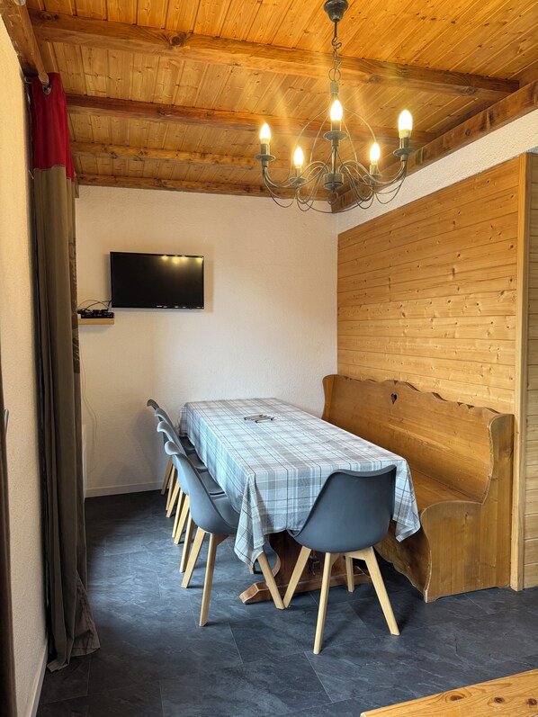 A dining area with a long table, chairs, a television, and a wooden bench.
