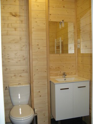 Un baño pequeño con paneles de madera, que incluye un inodoro, un lavamanos y un espejo.