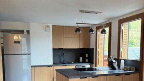 A modern kitchen with wooden cabinets, a stainless steel refrigerator, a black countertop, and a dining area with a wooden table and chairs.