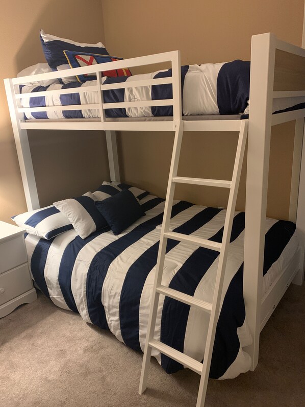 Una cama litera con escalera, ropa de cama a rayas y una mesita de noche.