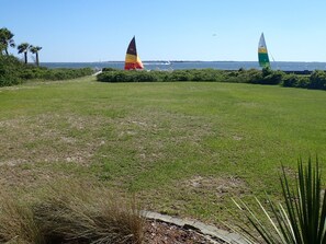 A grassy field with two sailboats on the water in the background.