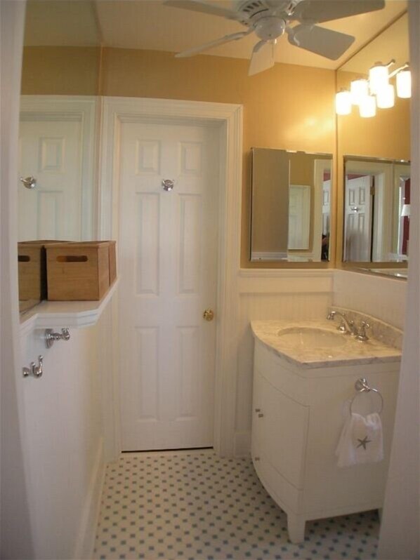 A bathroom with a white door, a vanity with a mirror, a sink, and a ceiling fan.