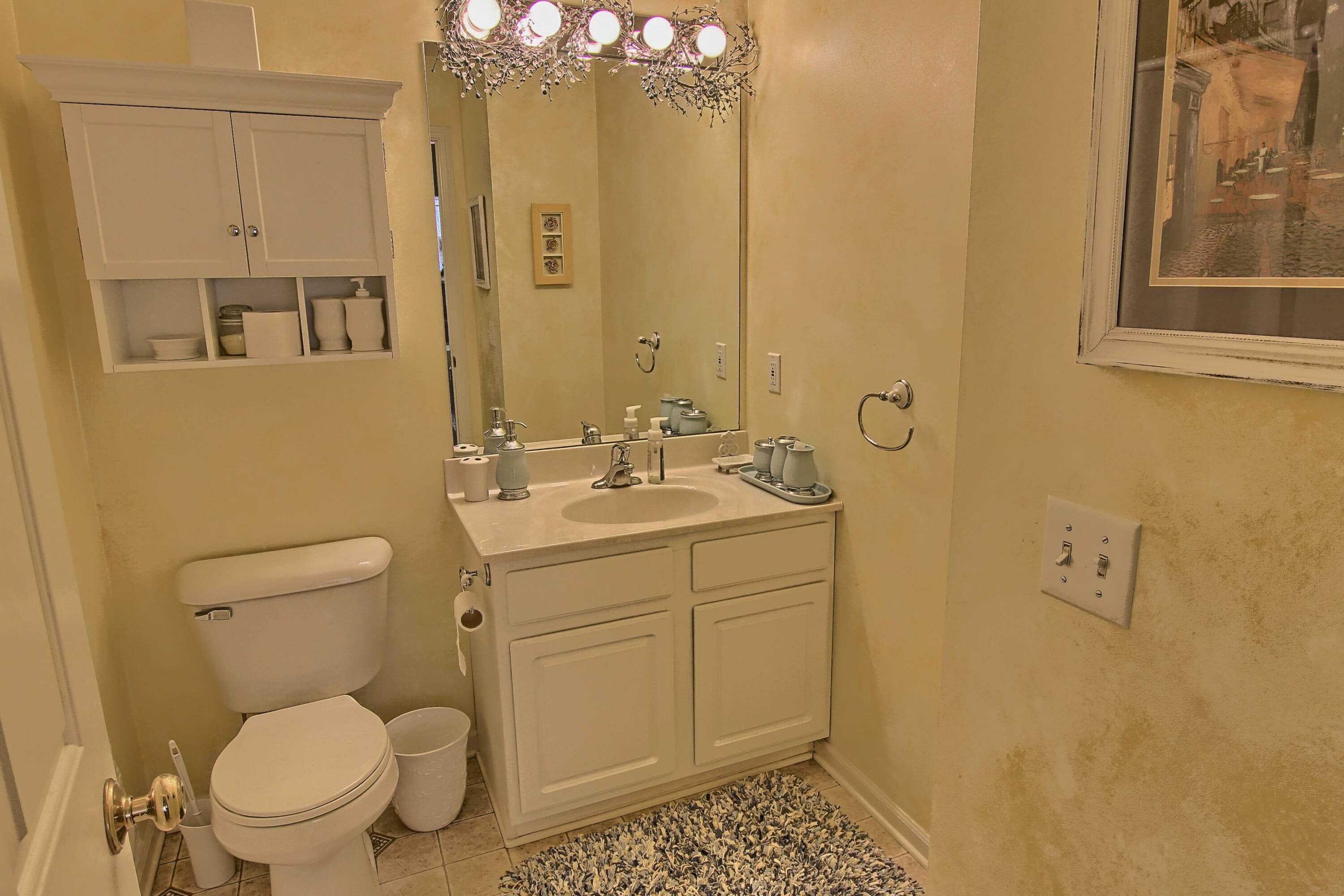 A bathroom with a toilet, sink, mirror, and cabinet.