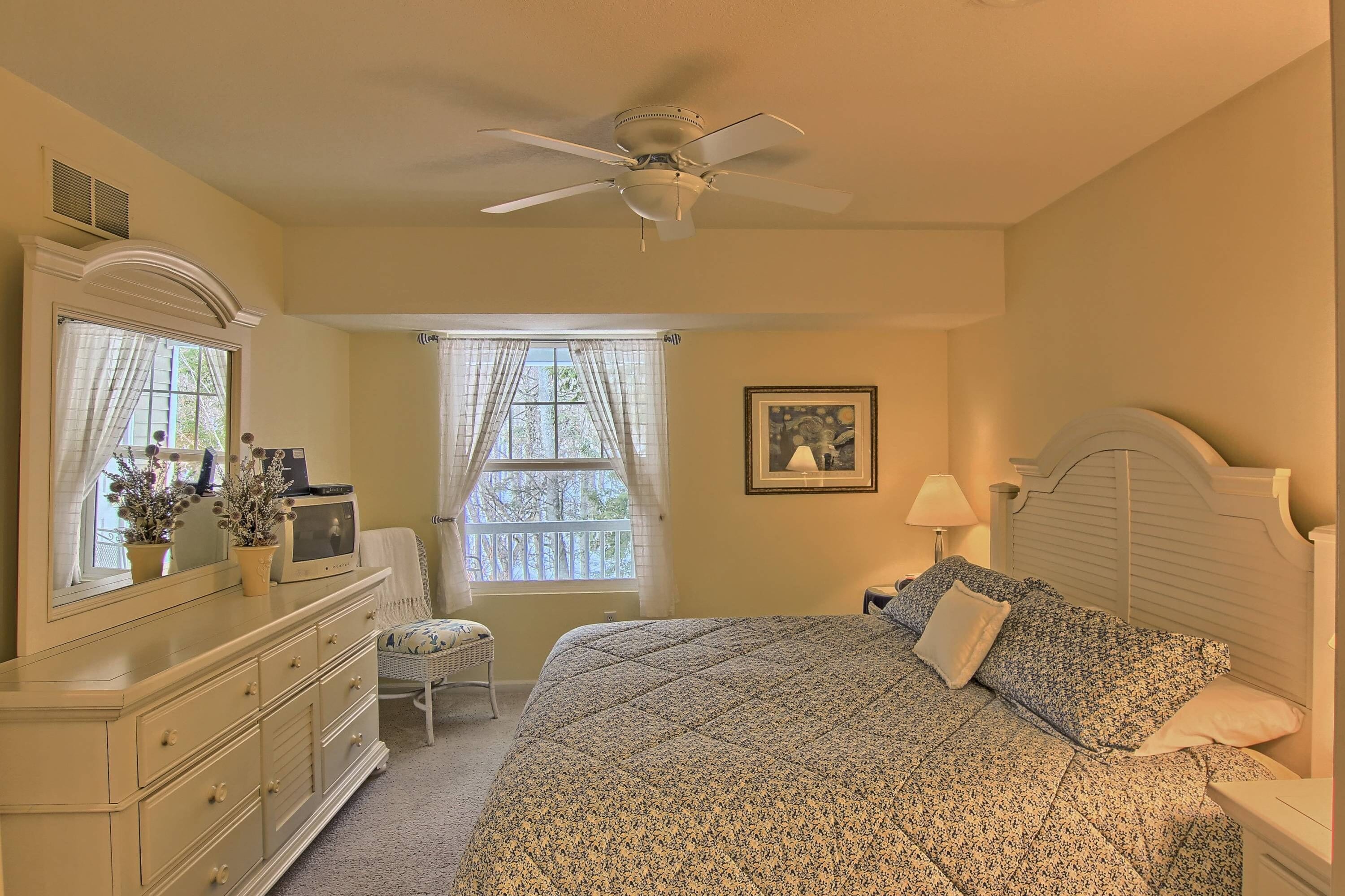 A bedroom with a bed, dresser, vanity, and a ceiling fan.