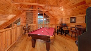 A wooden interior with a pool table, bar area, and a view through a window. - Couples | Honeymoon | Romantic Hot Tub (Gatlinburg)