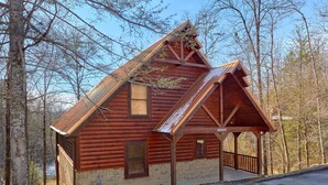 A log cabin with a steeply pitched roof, a front porch, and a small attached shed. - Couples | Honeymoon | Romantic Hot Tub (Gatlinburg)