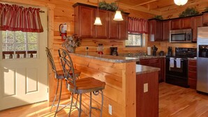 A wooden cabin kitchen with a bar area, wooden cabinets, a microwave, stove, and a blender. - Couples | Honeymoon | Romantic Hot Tub (Gatlinburg)