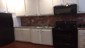 A kitchen with white cabinets, a black refrigerator, a microwave, and a stove.