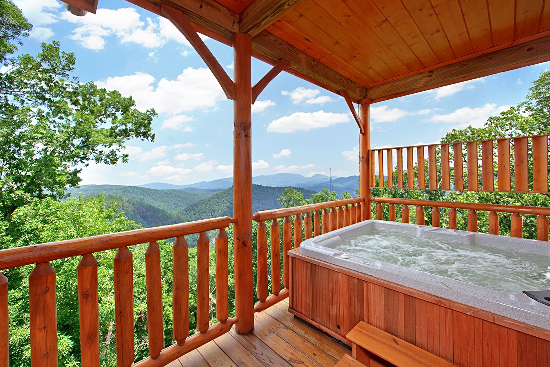 Una terraza de madera con un jacuzzi que da a un paisaje montañoso.