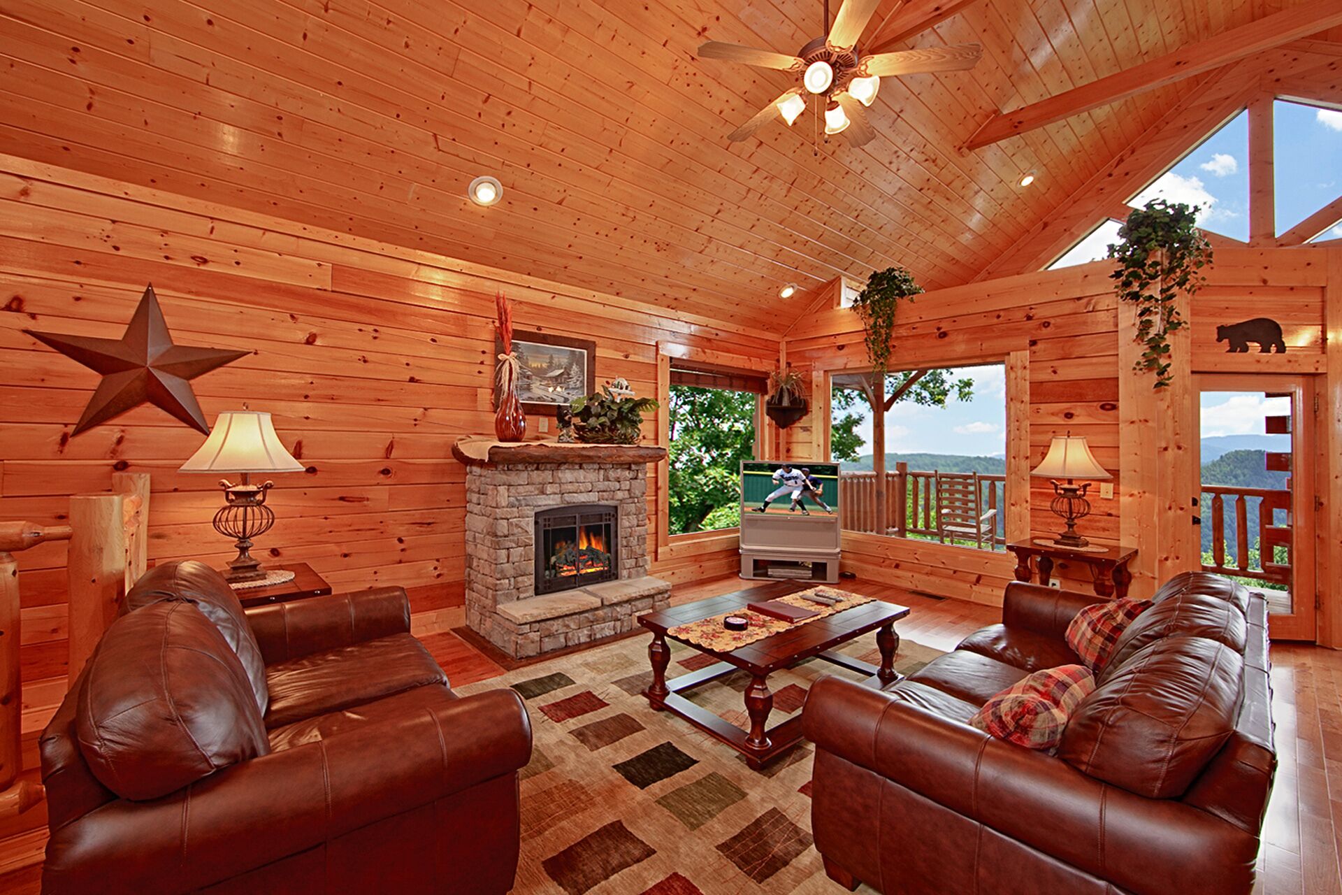 A cozy log cabin interior with a stone fireplace, leather sofas, and a television.