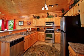 A kitchen with wooden cabinets, stainless steel appliances, granite countertops, and a decorative rug.