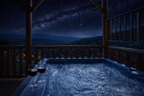 Un bain à remous avec deux verres de vin rouge sur un balcon, offrant une vue sur un ciel étoilé.