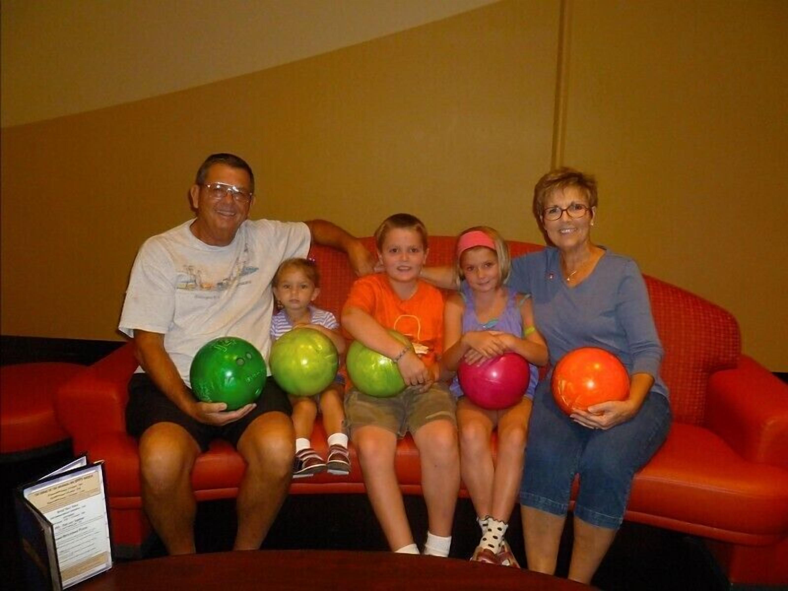 Une famille est assise sur un canapé rouge, avec des boules de bowling.