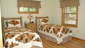 A bedroom with two beds, each with a quilted bedspread, wooden headboards, and a nightstand with a lamp.