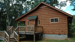 A wooden cabin with a porch, a small deck, and a satellite dish.