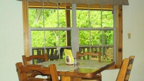 A wooden dining table with six chairs, set against a window with a view of greenery.