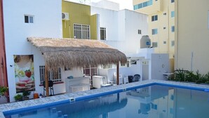 A swimming pool with a thatched roof seating area, surrounded by modern buildings with balconies. - STUNNING SKY DECK/FERRY & BEACH 2min/POOL/SLEEPS 5-16/24-7 SECURITY/GARDEN PATIO (Cancun)