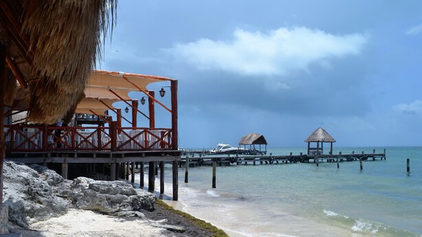 A beachside structure with a thatched roof, a wooden pier extending into the water, and a boat docked at the end. - STUNNING SKY DECK/FERRY & BEACH 2min/POOL/SLEEPS 5-16/24-7 SECURITY/GARDEN PATIO (Cancun)