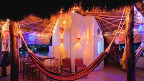 A hammock under a thatched roof with chairs and tables, suggesting a relaxing outdoor seating area. - STUNNING SKY DECK/FERRY & BEACH 2min/POOL/SLEEPS 5-16/24-7 SECURITY/GARDEN PATIO (Cancun)