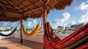 A rooftop terrace with multiple colorful hammocks hanging from the ceiling, a thatched roof, and a cityscape view in the background. - STUNNING SKY DECK/FERRY & BEACH 2min/POOL/SLEEPS 5-16/24-7 SECURITY/GARDEN PATIO (Cancun)