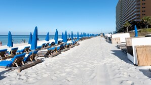 Ein Strand mit Reihen blauer Sonnenschirme und Holzliegestühlen.