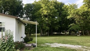 A white house with a covered porch, surrounded by a grassy yard and trees. - Newly remodeled, cozy cottage only steps away from the Katy Trail in Windsor, MO (Windsor)