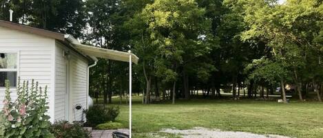 Een wit huis met een overdekte veranda, omgeven door een gazon en bomen.