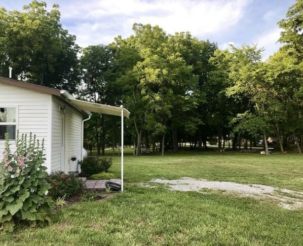 A white house with a covered porch, surrounded by a grassy yard and trees. - Newly remodeled, cozy cottage only steps away from the Katy Trail in Windsor, MO (Windsor)