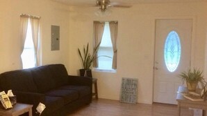 A living room with a dark-colored sofa, a small table, a ceiling fan, a potted plant, and a door with a stained glass window. - Newly remodeled, cozy cottage only steps away from the Katy Trail in Windsor, MO (Windsor)