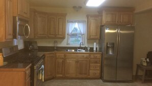 A kitchen with wooden cabinets, a stainless steel refrigerator, a stove, and a window with curtains. - Newly remodeled, cozy cottage only steps away from the Katy Trail in Windsor, MO (Windsor)