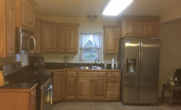 A kitchen with wooden cabinets, a stainless steel refrigerator, a stove, and a window with curtains.
