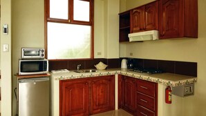 A kitchen with wooden cabinets, a microwave, a refrigerator, a window, and a fire extinguisher. - Galeodan Pompano Suite (Puerto Baquerizo Moreno)