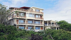 A multi-story building with balconies, large windows, and a view of surrounding greenery. - Galeodan Pompano Suite (Puerto Baquerizo Moreno)