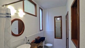 A bathroom with a wooden vanity, a white sink, a mirror, a toilet, and a shower curtain. - Galeodan Pompano Suite (Puerto Baquerizo Moreno)