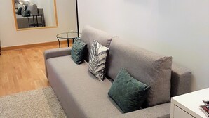 Una sala de estar con un sofá gris, una mesita redonda, un espejo y algunas fotos enmarcadas en la pared.