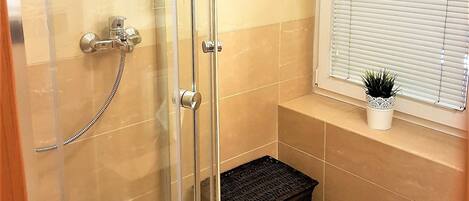 Un baño con cabina de ducha de vidrio, una cesta de mimbre negra y una pequeña planta en maceta sobre una estantería.