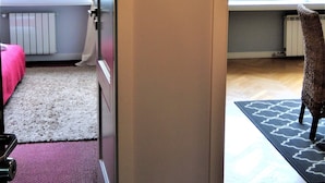Puerta abierta que da a una habitación con cama, radiador y ventana con cortinas.