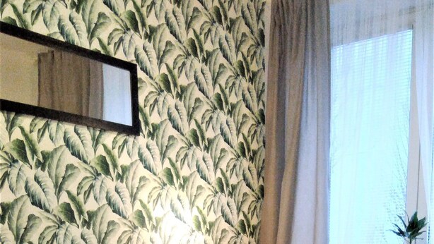Un dormitorio con una cama, una mesita de noche, una lámpara, una ventana con cortinas y una planta.