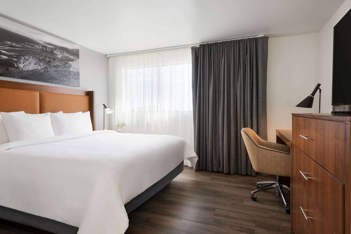 A hotel room with a large bed, a desk, a chair, a TV, and a window with curtains.