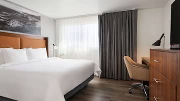 A hotel room with a large bed, a desk, a chair, a TV, and a window with curtains.