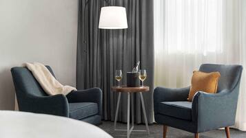 A hotel room with two armchairs, a small table with a lamp, and a bottle of wine.